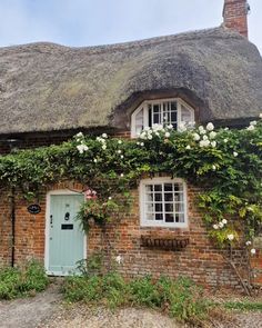 a thatched roof house with white flowers growing on the front door and window sill