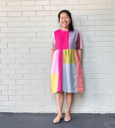 a woman standing in front of a white brick wall wearing a multicolored dress