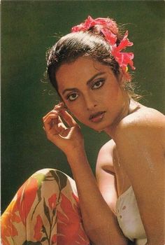 a woman with a flower in her hair is sitting on the ground and looking at the camera