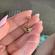 a woman's hand holding a gold bee belly ring