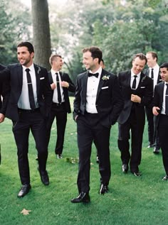 a group of men in tuxedos are walking through the grass