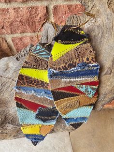 two pairs of multicolored fabric earrings hanging from a hook on a brick wall