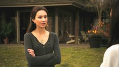 two women standing in front of a house with their arms crossed and looking at each other