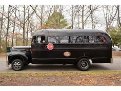 an old black bus is parked on the side of the road in front of some trees