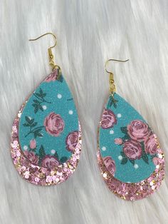 a pair of blue and pink earrings with roses on them sitting on top of a white fur