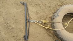 a tire with a rope attached to it sitting in the sand next to a metal hook