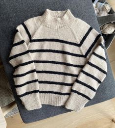 a white and black striped sweater sitting on top of a gray couch next to a pair of shoes