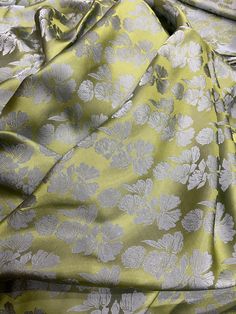 a yellow and grey flowered fabric with white flowers on it's side, laying on a bed