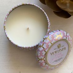 a white candle sitting next to a pink and gold tin on top of a table