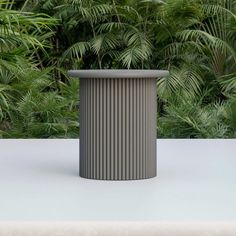 a grey trash can sitting on top of a white table in front of some plants