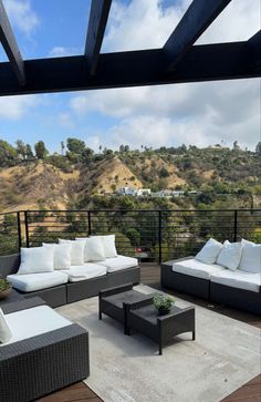 an outdoor living area with couches, tables and chairs on a deck overlooking the hills