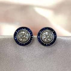 A stunning pair of halo studs. The centers of these studs feature approx. 0.50 carat round brilliant cut diamonds. Surrounding each diamond is a halo of natural French-cut blue sapphires. These earrings are platinum and push-backs. ✦ DIAMOND SPECIFICATIONS: Diamond Weight: Approx. 1.00 Carat Total Diamond Color: J Color Diamond Clarity: VS Clarity Diamond Cut: Round Brilliant Cut ✦ EARRING SPECIFICATIONS: Material: Platinum Stones: Diamond, Sapphire ✦ WHAT COMES IN YOUR SHIPMENT: - Your Engageme Luxury Halo Diamond Earrings With Round Cut, Luxury Round Cut Diamond Earrings With Halo Setting, Luxury Round Cut Halo Diamond Earrings, Classic Round Diamond Earrings With Halo, Classic Round Halo Diamond Earrings, Round Diamond Earrings With Halo Design For Anniversary, Round Halo Diamond Earrings, Round Cut Halo Diamond Earrings For Anniversary, Platinum Round Halo Diamond Earrings