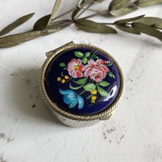 a ring with flowers painted on it sitting next to some leaves