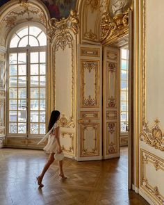 a woman walking through an ornately decorated room with gold and white decor on the walls