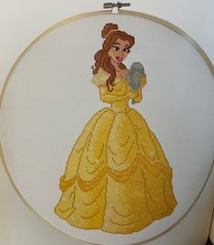 a cross stitch picture of a woman in a yellow dress holding a silver ball and wearing a tiara