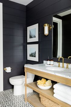 a white toilet sitting next to a sink in a bathroom under a large mirror with gold faucet