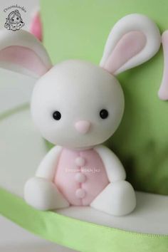 a small white rabbit figurine sitting on top of a green tablecloth covered cake