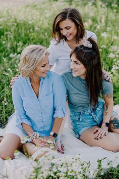 three women sitting in the grass with their arms around each other and smiling at one another