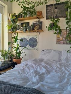 there is a bed with white sheets and plants on the wall above it in this bedroom