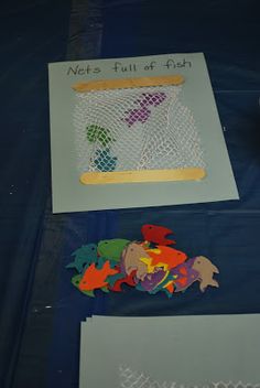 some paper cutouts are sitting on a blue tablecloth with writing and fish in the net