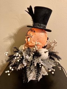 a black top hat with white flowers and greenery on a wooden table next to a wall