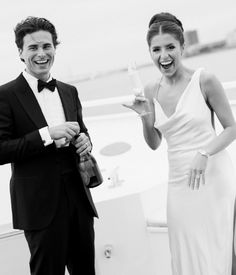 a man in a tuxedo and woman in a gown smile as they stand next to each other