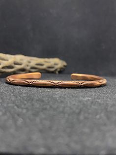 a pair of copper bracelets sitting on top of a stone floor next to a piece of driftwood