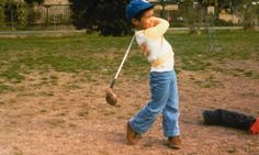 a young boy swinging a baseball bat at a ball on the ground in a park