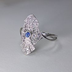 Art Deco Diamond & Blue Sapphire Fashion Ring, Filigree Design 14k White Gold DIAMOND DETAILS: Shape: Round Cut Diamonds Number of Stones: 44 Carats: 0.20 ct. Clarity: VS-SI - Eye Clean Color: H-I GEM STONES: Shape: Round Cut Blue Sapphire Number of stones: 1 Approx. 0.05 ct. Clarity: Eye Clean Color: Medium Blue SETTING: Material: 14k White Gold (Available Also in 14K Yellow Gold or 14K Pink Gold - No Extra Charge) Ring size 7 (custom made in other sizes) Comes packaged In Pop up gift box S Art Deco 14k White Gold Rings With Gemstone, Art Deco Blue Platinum Ring, Art Deco Oval Diamond Ring With Accent Stones, Blue Art Deco Diamond Ring With Diamond Cut, Sapphire And Diamond Accented Platinum Jewelry, Art Deco Blue Diamond Ring With Accents, Blue Art Deco Diamond Ring With Accents, Art Deco Blue Round Cut Ring, Blue Art Deco Ring With Round Cut