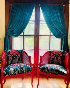 two red chairs sitting next to each other in front of a window with blue curtains