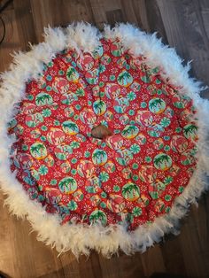 a red and white round cushion with feathers on it sitting on a wooden floor next to a lamp