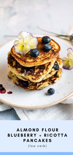 blueberry and ricotta pancakes are stacked on a plate with flowers in the background