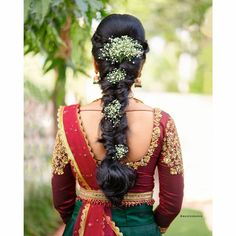 a woman wearing a green and red sari with flowers in her hair is seen from the back