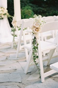 the chairs are decorated with flowers and greenery for an outdoor wedding ceremony in white