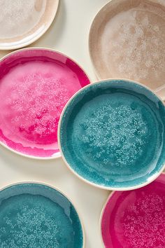 four different colored bowls are sitting on a white surface with pink, blue and green speckles