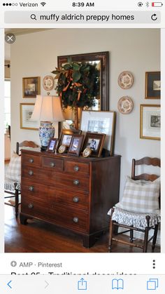 a living room filled with furniture and pictures on top of a wooden dresser next to a lamp