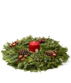 a christmas wreath with pine cones and red candle on it, surrounded by evergreen branches