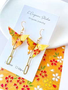 a pair of yellow origami bird earrings sitting on top of a white plate