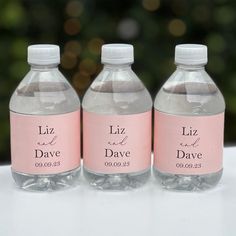 three water bottles with labels on them sitting next to each other, one pink and the other white