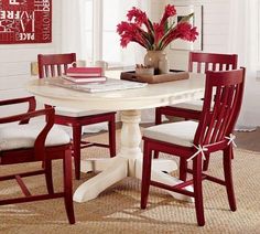 a white table with red chairs around it and a vase full of flowers on top