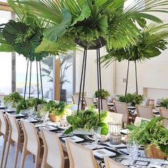 a dining room table set with place settings and large palm trees in the centerpieces