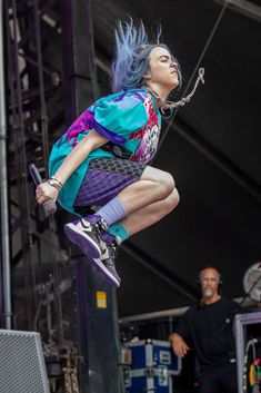 a person jumping in the air on a skateboard at a music festival with other people watching