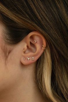 a woman wearing gold ear piercings with small white pearls on the side of her ear