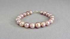 "Large freshwater pearl beads in lustrous light pink with a sterling silver lobster clasp and soldered closed jump ring closure. A lovely classic style for weddings, date nights, work days, and casual around-town trips. These 10 to 11 mm off round, banded pearls are so much more than just pink. They have mauve and lavender tones as well. Choose from several lengths or request a custom size: Child (XXSmall) -- 6\" (15 cm) Extra Small -- 6.5\" (16.5 cm) Small -- 7 3/8\" (18.5 cm) Medium -- 7 3/4\" Pearl Bead Bracelet, Peacock Pearl, Freshwater Pearl Drop Earrings, Freshwater Pearl Jewelry, Buy Bead, Everyday Gifts, Pearl Design, Bracelet Sterling Silver, Bead Jewelry