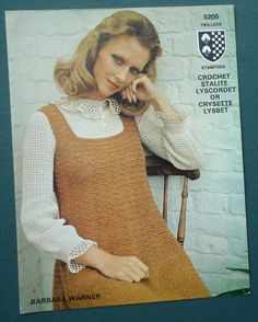 a woman is posing for a photo in a knitted sweater and overalls, with her hand on her chin