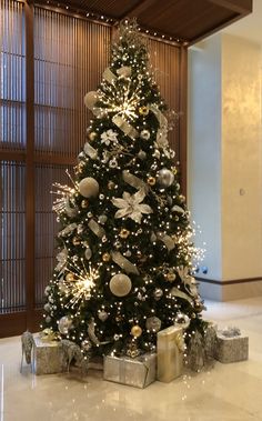 a decorated christmas tree in a lobby with presents under it and lights on the top