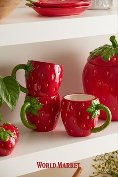 red ceramic strawberry cups and saucers on white shelves with strawberries in the background