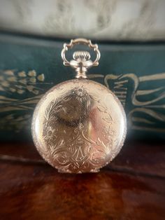 This pocket watch is in excellent antique condition. The gold fill is entirely intact and the watch runs perfectly. There are minor surface scratches indicative of age. The front of this piece is covered in stunning engravings and has the letter "A" at the bottom. The back mirrors the front in design but does not have the A.  The back panel opens to reveal the name Anna Bowman and the year 1911. The back panel does occasionally pop open a little but doesn't effect wear.  It weighs 37.4 grams and Victorian Yellow Gold Pocket Watch For Anniversary, Heirloom Engraved Yellow Gold Pocket Watch, Victorian Yellow Gold Pocket Watch Collectible, Victorian Yellow Gold Pocket Watch For Collectors, Gold Victorian Style Pocket Watch For Formal Occasions, Victorian Engraved Gold Watches, Timeless Yellow Gold Pocket Watch With Locket, Heirloom Gold Engraved Watch, Formal Yellow Gold Pocket Watch With Locket