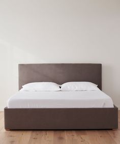 a bed with white sheets and pillows on top of wooden flooring in a room