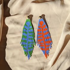 two pairs of colorful beaded earrings sitting on top of a white cloth covered bag